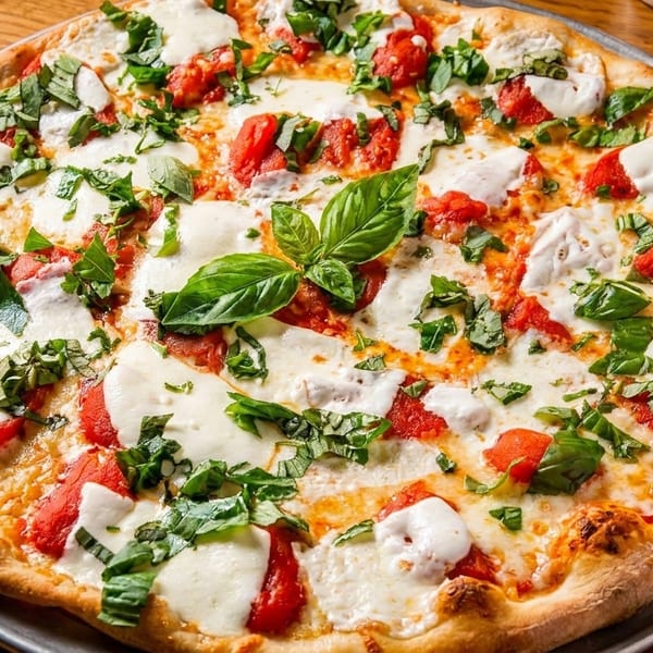 Freshly baked Margherita pizza with melted mozzarella, red tomato sauce, and green basil leaves.